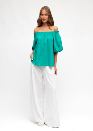 Woman wearing a green off-shoulder top and white pants on a white background