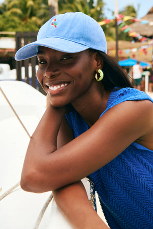 Woman wearing a blue cap and blue top, smiling outdoors with blurred background
