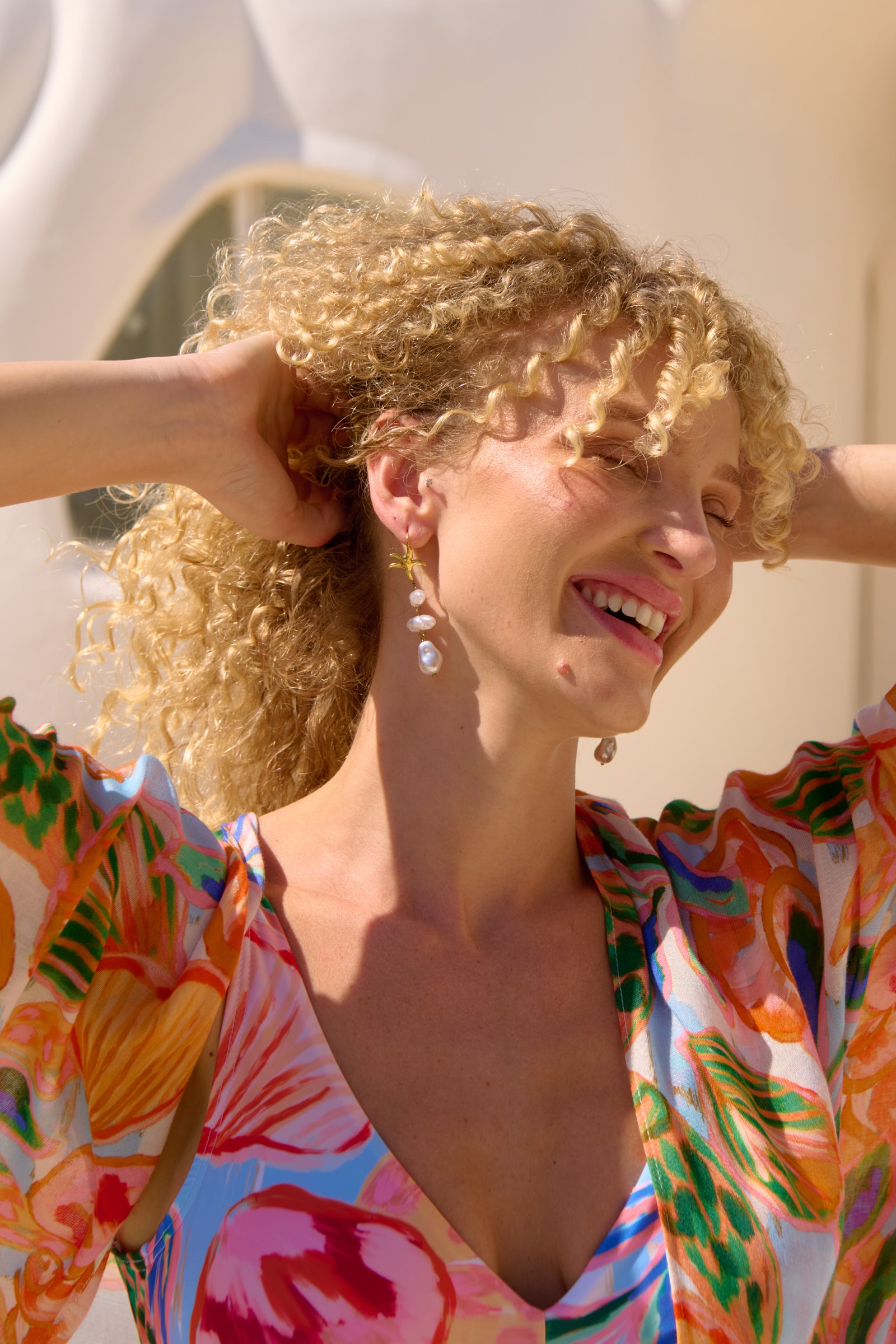 Woman with curly blonde hair wearing a colorful floral dress against a white background