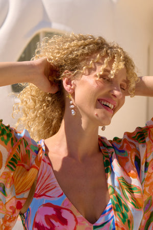 Woman with curly blonde hair wearing a colorful floral dress against a white background