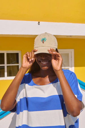 Person wearing a beige cap with a palm tree design against a yellow building.