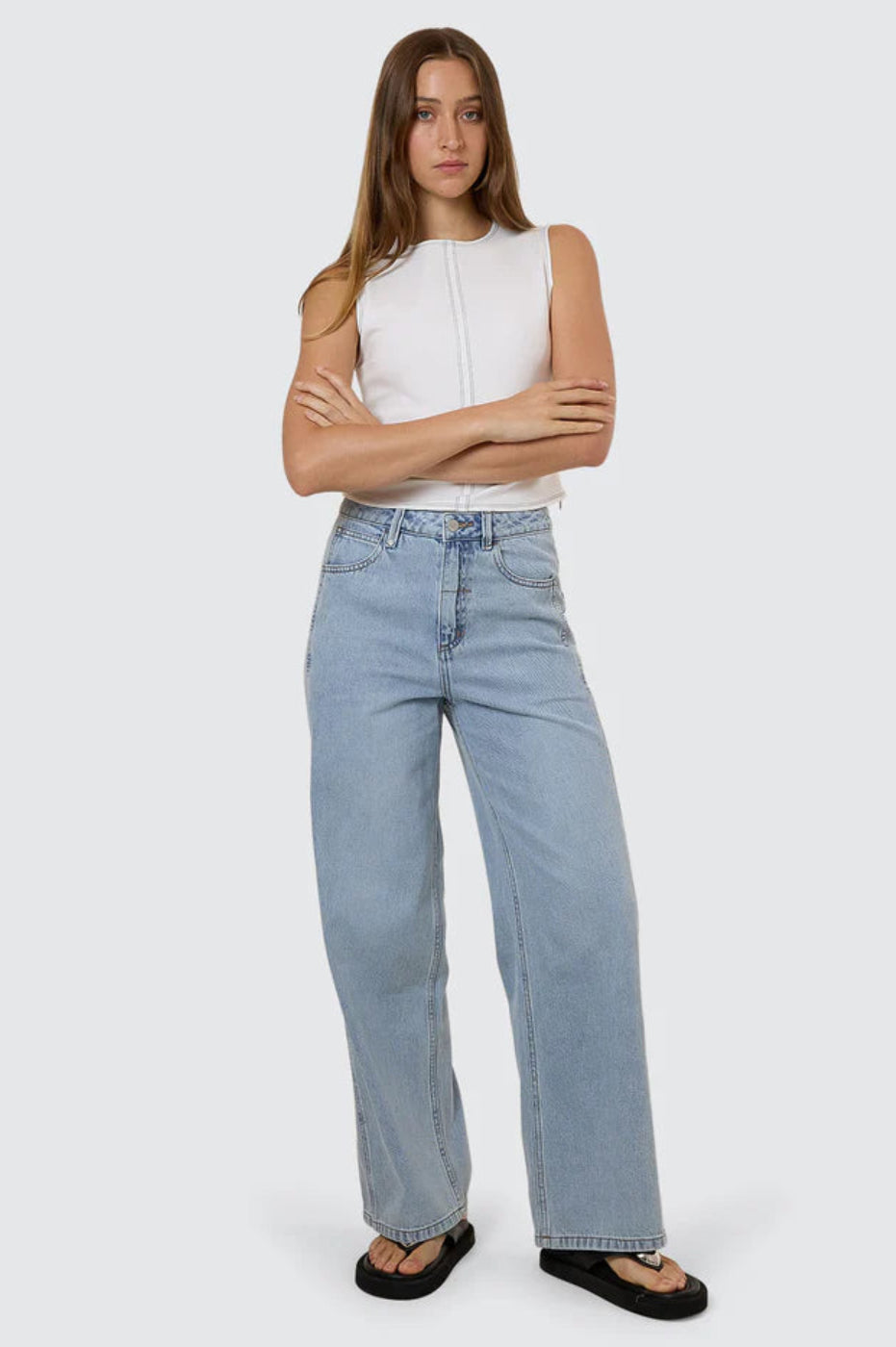 Woman wearing a white sleeveless top and light blue jeans on a plain background