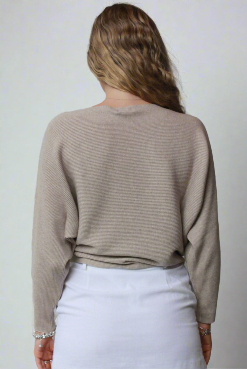 A beige knit sweater worn over a white skirt by a woman, with her arms at her sides and a neutral expression on her face.