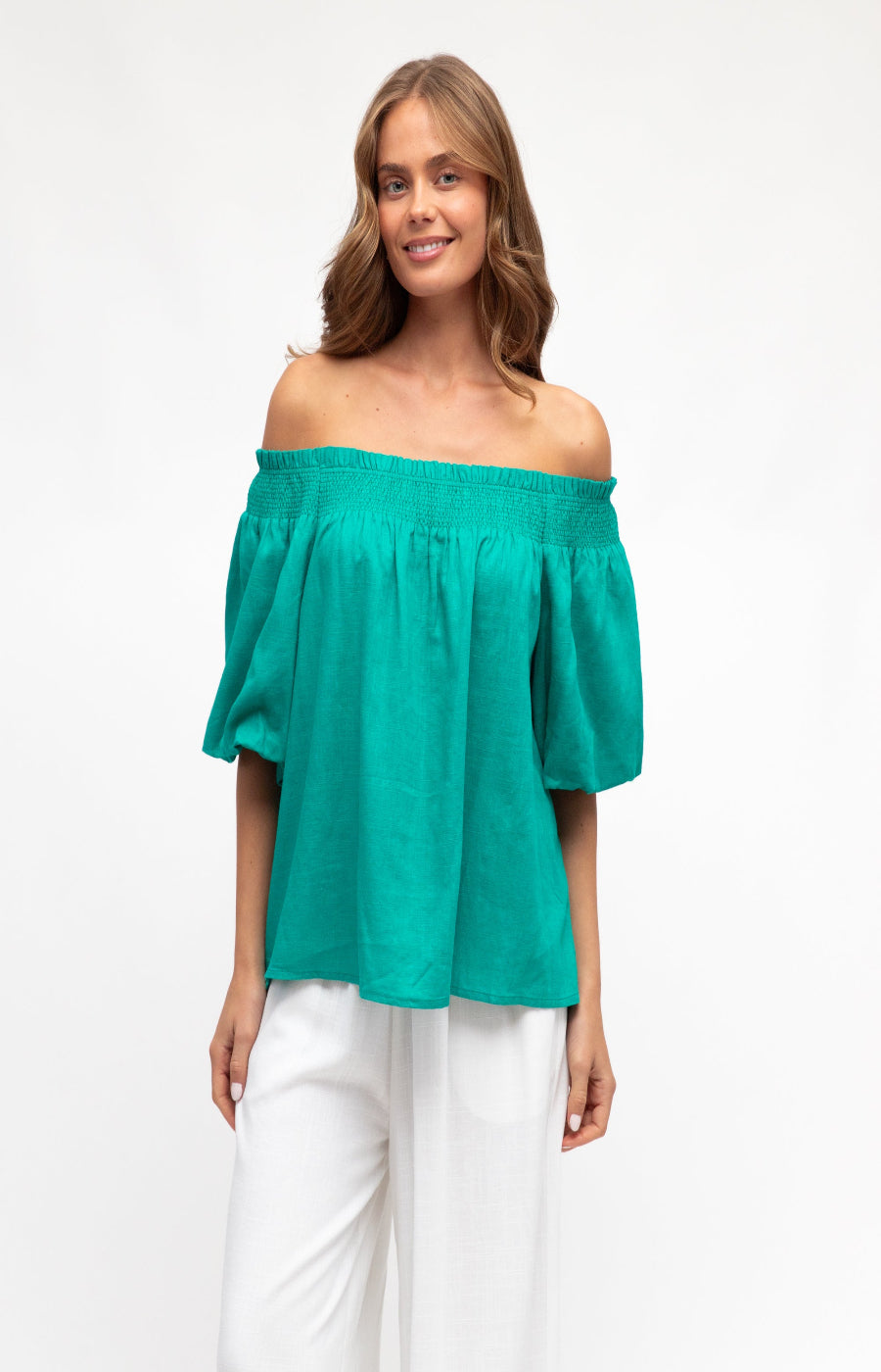 Woman wearing a teal off-shoulder top and white pants on a white background