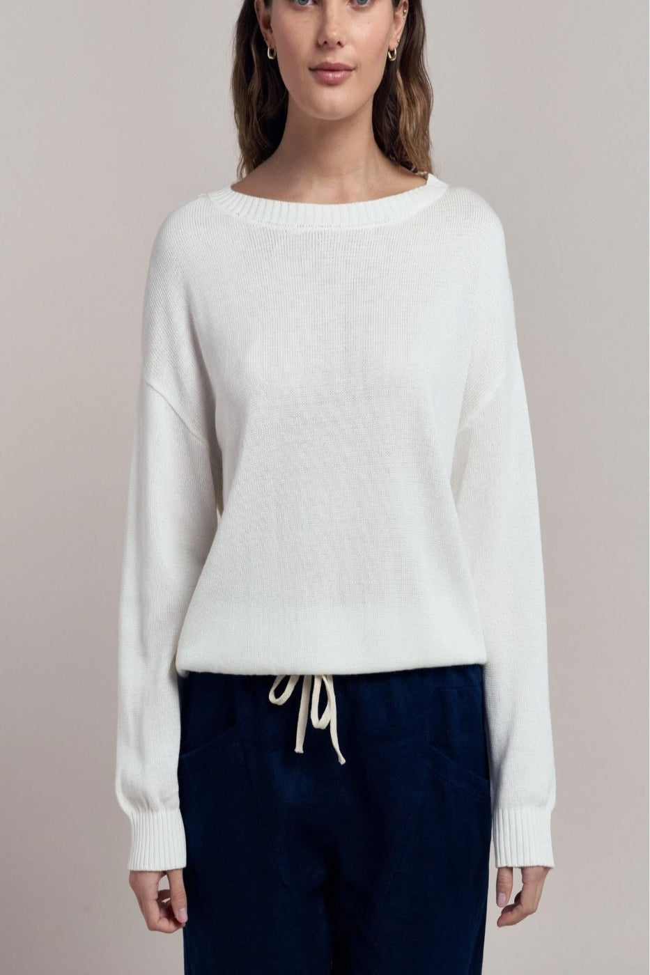 Woman wearing a white sweater with navy pants on a beige background