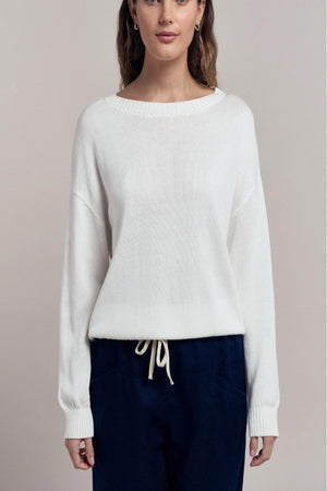 Woman wearing a white sweater with navy pants on a beige background